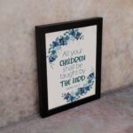 Christian wall art of Isaiah 54:13 with blue text surrounded by a wreath of blue flowers and green leaves on a cream background. Wall Art displayed on the wall in a black frame