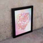 Let Your Faith Be Bigger Than Your Fear Christian wall art with pink and red script font and pastel watercolor background. Wall Art displayed on the wall in a black frame