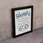 Infidu Matthew 5:8 Christian wall art with blue text on a white background, featuring a subtle pastel floral design and stylized GOD. Wall Art displayed on the wall in a black frame