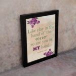 Infidu Jeremiah 18:6 Christian wall art with green and purple text on a light beige background, decorated with purple flowers in the corners. Wall Art displayed on the wall in black frame