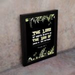 The Lord of Hosts is With Us Psalm 46:7 Bible Verse Wall Art with green leaves and bold cream and white text. displayed on the wall in a black frame