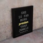 Proverbs 31:10 wall art with precious gold on a black background, featuring minimalist design and modern font. displayed on the wall in a black frame