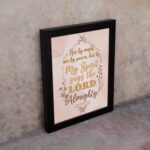 Zechariah 4:6 Christian wall art featuring Not By Might Nor By Power in gold script on a light peach background with floral accents. Wall Art displayed on the wall in a black frame