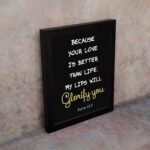 Psalm 63:3 Bible verse wall art with a dark background and cursive Glorify You in light gold. Christian home decor by Infidu. Wall Art kept on the wall in a black frame