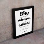 Proverbs 31:26 Bible wall art featuring bold and simple fonts on a white background, framed in black, highlighting the message of wisdom. displayed on the wall in a black frame