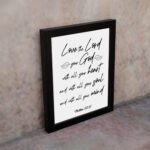 Matthew 22:37 Bible wall art with black text on a white background, featuring Love the Lord your God in cursive letters. displayed on the wall in a black frame