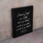 Matthew 22:37 Bible wall art with white text on a black background, reading Love the Lord your God with all your heart. displayed on the wall in a black frame