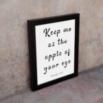 Keep Me As The Apple Of Your Eye Psalm 17:8 black text in cursive on a white background, framed in black displayed on the wall in a black frame- Christian wall art