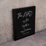 The Lord My God Lights Up My Darkness Psalm 18:28 white handwritten text on black background Christian wall art displayed on the wall in a black frame