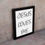 Jesus Loves Me Bible wall art with black script text on a white background. Wall Art hung on the displayed in a black frame