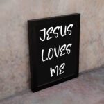 Jesus Loves Me Bible wall art with bold gold text and a decorative gold border on a black background. Wall Art displayed on the wall in a black frame