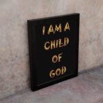 I Am A Child Of God Bible wall art with bold golden yellow text on a black background. Wall Art displayed on the wall in a black frame