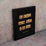 Be Still and Know That I Am God - Psalm 46:10 Bible Verse Wall Art with Scrabble-like Letters on Dark Background Wall Art displayed on the wall in a black frame