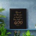 Infidu wall art with the text Blessed is the pure in heart, for they shall see God in gold font on a black background. displayed on the wall in a black frame