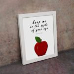 Keep Me As The Apple Of Your Eye" Psalm 17:8 Bible Wall Art featuring a red apple and white background. Perfect Christian home decor. Wall Art displayed on the wall in white frame