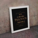 Black wall art with gold text saying SHE IS FAR MORE PRECIOUS THAN JEWELS from Proverbs 31:10, styled with decorative elements. displayed on the wall in a white frame