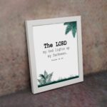 The Lord My God Lights Up My Darkness Psalm 18:28 Bible Verse Wall Art with black text and green tropical leaves on a white background. Wall Art displayed on the wall in a white frame