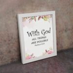 With God All Things Are Possible Matthew 19:26 Bible Verse Wall Art with black text and floral accents in pink and green on a white background. Wall Art displayed on the wall in a white frame