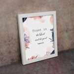 Trust In The Lord And Do Good Psalm 37:3 Bible Verse Wall Art with watercolor and floral designs on a white background. Wall Art displayed on the wall in a white frame