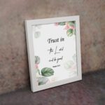 Trust in the Lord and Do Good Psalm 37:3 Bible Wall Art with botanical green leaves and pink flowers on a white background. Wall Art displayed on the wall in a white frame