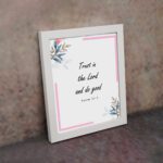 Infidu Bible wall art featuring Psalm 37:3 in black text with blue and pink floral accents and a soft pink border. Wall Art displayed on the wall in a white frame