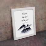 Infidu Trust In The Lord And Do Good Psalm 37:3 Bible Wall Art with black text and mountain illustration. Wall Art displayed on the wall in a white frame