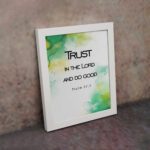 Trust in the Lord and Do Good Psalm 37:3 Bible Verse Wall Art with watercolor green and yellow background. Wall Art displayed on the wall in a white frame