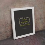 Psalm 46:1 Bible Wall Art with muted text on a dark gray background, featuring varying fonts and sizes. Wall Art displayed on the wall in a white frame