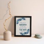 Christian wall art of Isaiah 54:13 with blue text surrounded by a wreath of blue flowers and green leaves on a cream background. Wall Art displayed on the wall in a black frame