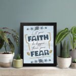 Infidu Let Your Faith Be Bigger Than Your Fear Hebrews 13:6 Christian Wall Art with blue and yellow floral design Wall Art displayed on the table in a black frame