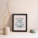 Christian wall art with greenish-blue 'Faith' and 'Fear' text on a light peach floral background. Wall Art displayed on the wall in a black frame