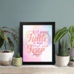 Let Your Faith Be Bigger Than Your Fear Christian wall art with pink and red script font and pastel watercolor background. Wall Art displayed on the table in a black frame