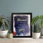 Infidu Matthew 5:8 Christian wall art with yellow text on a dark blue textured background, featuring bright yellow 'GOD' and a hint of red floral design. Wall Art displayed on the table in black frame