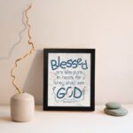 Infidu Matthew 5:8 Christian wall art with blue text on a white background, featuring a subtle pastel floral design and stylized GOD. Wall Art displayed on the wall in a black frame