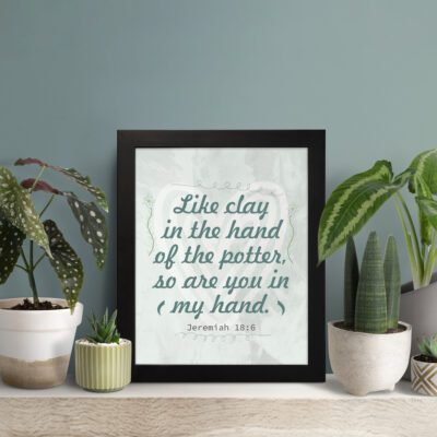 Infidu Jeremiah 18:6 Christian wall art with dark green cursive text on a light gray textured background, framed with decorative details. Wall Art displayed on the table in a black frame