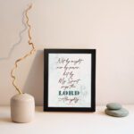 Zechariah 4:6 Christian Wall Art with minimalist design, dark brown text, and teal LORD on a light white floral background. Wall Art displayed on the wall in a black frame