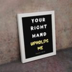 Infidu Your Right Hand Upholds Me Psalm 63:8 Bible Wall Art with a black background, yellow, and white font and white frame on the wall