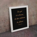 Bible verse wall art with Psalm 115:3 in gold text on a black background. Simple, elegant font centered for easy readability. displayed on the wall in a white frame