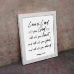 Matthew 22:37 Bible wall art with black text on a white background, featuring Love the Lord your God in cursive letters. displayed on the wall in a white frame