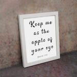 Keep Me As The Apple Of Your Eye Psalm 17:8 black text in cursive on a white background, framed in black displayed on the wall in a white frame- Christian wall art