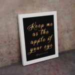 Keep Me As The Apple Of Your Eye Psalm 17:8 gold cursive text on black background - Christian wall art for home decor displayed on the wall in a white frame