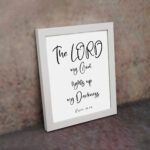 The Lord My God Lights Up My Darkness Psalm 18:28 white text on a black background with a black frame Christian wall art. displayed on the wall in a white frame