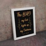 The Lord My God Lights Up My Darkness Psalm 18:28 gold text on black background Christian wall art displayed on the wall in a white frame