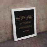 With God, All Things Are Possible Matthew 19:26 gold script on black background Christian wall art displayed on the wall in a white frame