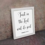 Trust In The Lord And Do Good Psalm 37:3 black cursive text on white background Christian wall art displayed on the wall in a white frame