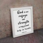 Psalm 46:1 Bible wall art with black bold text on a white background, saying 'God is our refuge and strength, a very present help in trouble. Wall Art displayed on the wall in a white frame