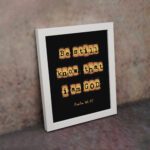 Be Still and Know That I Am God - Psalm 46:10 Bible Verse Wall Art with Scrabble-like Letters on Dark Background Wall Art displayed on the wall in a white frame