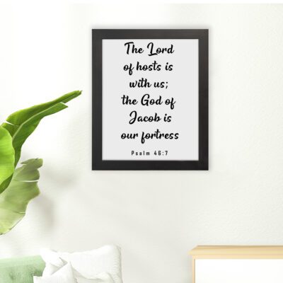 The Lord Of Hosts Is With Us - Psalm 46:7 Bible Verse Wall Art with White Text on Light Background Framed in Black Wall Art displayed on the wall in a black frame