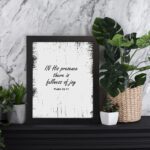 In His Presence There Is Fullness of Joy - Psalm 16:11 Bible Verse Wall Art with Bold Black Text and Distressed Edges on White Background Wall Art displayed on the table in a black frame