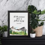 In His Presence There Is Fullness of Joy - Psalm 16:11 Bible Verse Wall Art with Mountains and Trees on White Background Wall Art displayed on the table in a black frame